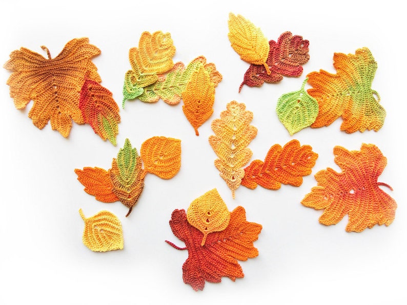 Puede incluir: Una colecci&oacute;n de hojas de oto&ntilde;o de ganchillo en varios tonos de naranja, amarillo y verde. Las hojas est&aacute;n dispuestas sobre un fondo blanco.