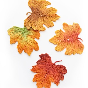 Puede incluir: Cuatro hojas de oto&ntilde;o de ganchillo en tonos de naranja, amarillo y verde. Las hojas est&aacute;n dispuestas sobre un fondo blanco.
