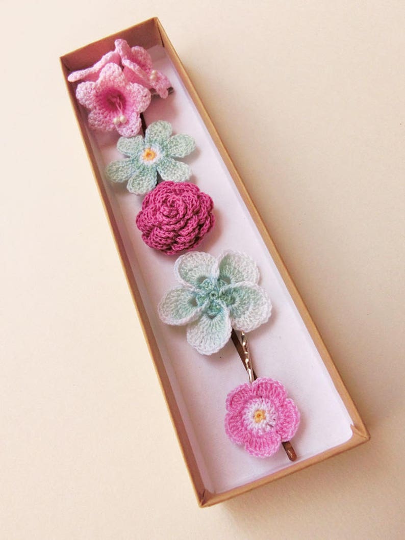 May include: A set of six crocheted flower hair clips in a brown box. The flowers are in shades of pink and green.