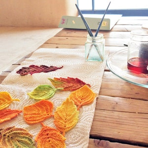 Puede incluir: Hojas de ganchillo en varios tonos de naranja, amarillo y verde est&aacute;n dispuestas sobre una toalla de papel blanca. Dos pinceles est&aacute;n en un frasco de vidrio, y dos frascos de l&iacute;quido est&aacute;n sobre una mesa de madera.