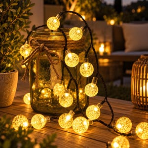 Puede incluir: Una cadena de luces LED esférica de luces LED brillantes con una textura de vidrio agrietado. Las luces están conectadas por un cable negro fino y se encuentran dispuestas alrededor de un frasco de vidrio transparente grande con un lazo de cuerda de yute.