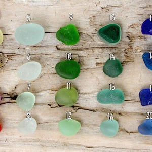Puede incluir: Surtido de veinte piezas de vidrio de mar en varios colores, incluyendo amarillo, verde, azul y morado. El vidrio de mar se exhibe sobre una superficie de madera envejecida, mostrando sus formas suaves y redondeadas.