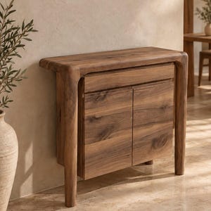 May include: A wooden console table featuring a smooth, rounded top edge and four sturdy legs. The piece includes a single horizontal drawer positioned above two cabinet doors, all showcasing a natural wood grain finish with brown tones.