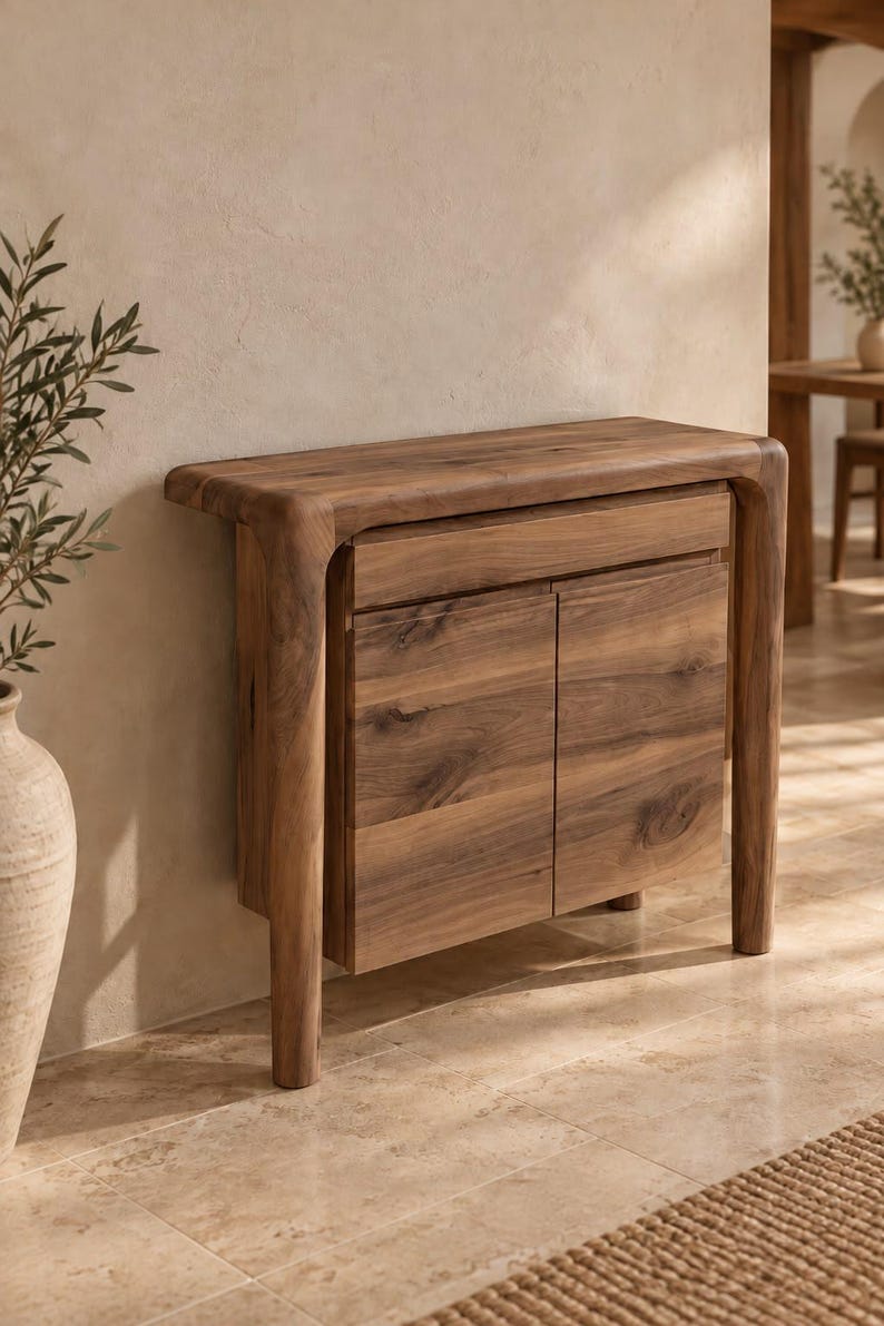 May include: A wooden console table featuring a smooth, rounded top edge and four sturdy legs. The piece includes a single horizontal drawer positioned above two cabinet doors, all showcasing a natural wood grain finish with brown tones.