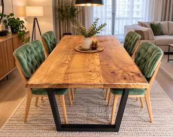 May include: A rectangular dining table with a natural wood grain top and black metal U-shaped legs, surrounded by four green tufted upholstered chairs with light wood frames. A white vase and two small candles sit on a round woven tray.