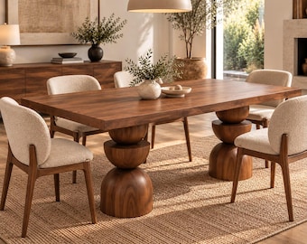 May include: A rectangular wooden dining table with a thick top and two sculptural pedestal bases made of stacked wooden spheres. The table is surrounded by six chairs with light-colored textured upholstery and dark wooden frames.