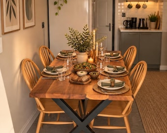 May include: A wooden dining table with a live edge and black X-shaped metal legs, surrounded by four light-colored wooden spindle-back chairs. The table is set with white plates, green napkins, glassware, and a central bowl of salad.