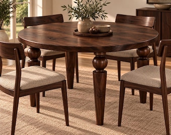 May include: A round dark wood dining table with four thick, ball-accented legs. Four chairs with dark wood frames and textured beige upholstered seats are arranged around the table. A wooden tray holds a vase with greenery and small bowls.