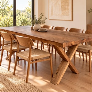 Puede incluir: Una mesa de comedor rectangular de madera con una superficie gruesa y texturizada y una base robusta en forma de X, acompañada de seis sillas de madera a juego con asientos trenzados. El conjunto es de madera natural.