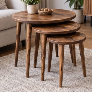 May include: A set of three round nesting tables crafted from dark brown wood with visible grain patterns. Each table features three tapered legs and a smooth circular top, arranged in a cascading formation from largest to smallest.