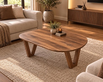 May include: A low-profile coffee table with a smooth, oval-shaped wooden top featuring a rich brown grain pattern. The table is supported by four angled, V-shaped wooden legs that provide a stable base for the tabletop surface.