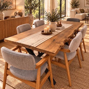 Peut inclure: Une table à manger rectangulaire avec un plateau en bois brut à bords naturels et des pieds en métal noir, entourée de six chaises avec assises rembourrées gris clair et structures en bois. Un chemin de table beige porte un plateau en bois.