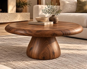 May include: A round, low-profile coffee table crafted from dark brown wood with a prominent grain pattern. The table features a thick, circular tabletop supported by a wide, tapered pedestal base that narrows toward the floor.