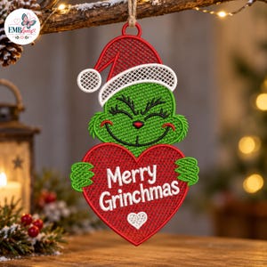May include: A green embroidered character ornament wearing a red and white Santa hat, holding a large red heart with the white text Merry Grinchmas and a small white heart icon below the text, suspended by a jute twine loop for hanging.