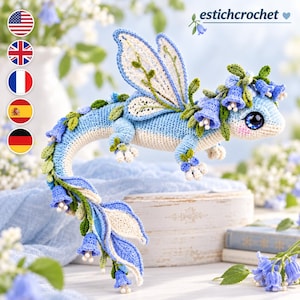 May include: A crochet dragon figurine in shades of light blue, cream, and green. The creature features lace-like wings, a long tail, and a head adorned with blue bell-shaped flowers. It has large, dark, expressive eyes and small white claws.