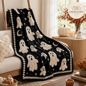 May include: A black crochet blanket featuring a repeating pattern of cream-colored ghosts, crescent moons, and small stars. The blanket has a decorative cream-colored border with a scalloped edge, showcasing intricate yarn work and texture.