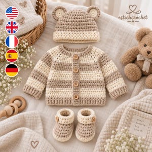 May include: A crochet set featuring a beige and cream striped long-sleeve cardigan with four wooden buttons, a matching beanie with bear ears, and a pair of booties with side buttons. The set is displayed alongside a brown plush teddy bear.