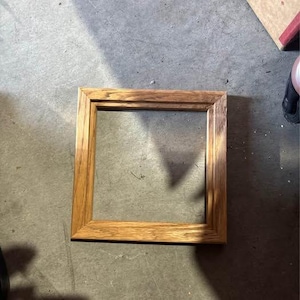 May include: A square wooden picture frame with a natural light brown wood grain finish. The frame features a simple, clean-lined design with mitered corners and a flat, smooth surface profile, showcasing the organic texture of the wood throughout.