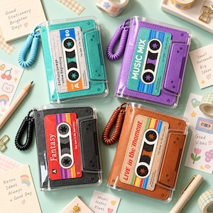 May include: Four rectangular notebooks with clear plastic covers, each featuring a cassette tape graphic. The notebooks come in teal, purple, black, and brown, and include a matching coiled plastic wrist strap attached to the side.