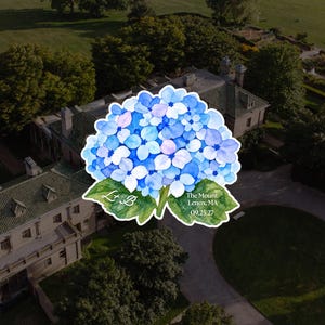 May include: A watercolor illustration of a blue and purple hydrangea flower with green leaves. The left leaf features the initials L+B, and the right leaf displays the text The Mount, Lenox, MA, 09.25.27 in white lettering.