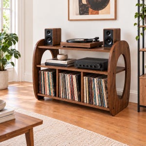 May include: A wooden media console with rounded side panels featuring three lower storage compartments filled with vinyl records, a middle shelf holding a turntable and amplifier, and two speakers placed on the top surface.