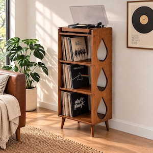 Könnte beinhalten: Ein hoher Schallplattenspieler-Ständer aus braunem Holz mit drei Regalböden zur Aufbewahrung von Vinylplatten. Die Seitenteile haben tropfenförmige Ausschnitte. Ein Plattenspieler steht oben auf, und die Regale sind mit Vinylalben gefüllt.