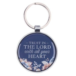 May include: A circular metal keychain featuring a dark blue background with the white text "TRUST IN THE LORD with all your HEART" printed in the center. The bottom of the circular design is decorated with a floral pattern in shades of orange and blue.