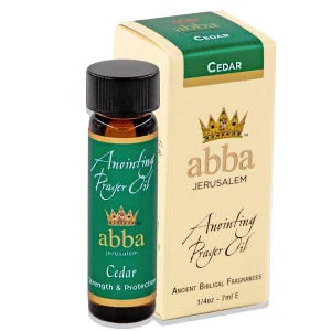 May include: A small glass bottle of Abba Jerusalem Cedar anointing prayer oil with a black cap, featuring a green label with a crown logo and the text Strength & Protection. Beside it stands a matching cream-colored box labeled 1/4oz - 7ml E.