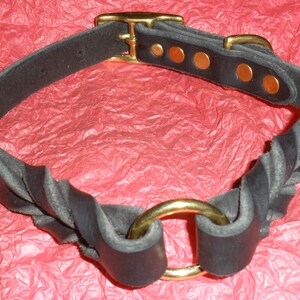 Puede incluir: Un collar de cuero negro con un dise&ntilde;o trenzado, asegurado con una hebilla y herrajes de lat&oacute;n. El collar incluye un anillo central de lat&oacute;n y est&aacute; sujeto con varios remaches de lat&oacute;n a lo largo de la correa, creando un accesorio resistente.