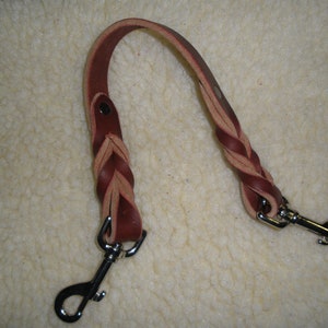 May include: A braided leather dog leash in shades of brown and tan. The leash features a sturdy metal clasp at each end for secure attachment. The braided section adds a decorative touch to this pet accessory.