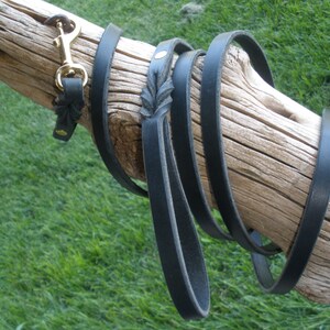 K&ouml;nnte beinhalten: Eine schwarze Lederhundeleine mit einem Messingverschluss und einem dekorativen Design am Griff.