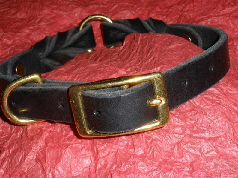Puede incluir: Un collar de cuero negro que presenta una secci&oacute;n trenzada y una secci&oacute;n de correa lisa. El collar se asegura con una hebilla de metal dorado pulido e incluye una anilla en D dorada a juego. Los herrajes est&aacute;n fijados con remaches dorados.