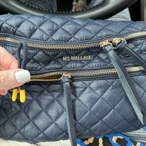 May include: A navy blue quilted crossbody bag with gold zippers and a leather strap. The bag has the text "MZ WALLACE" printed on the front.