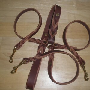 Pu&ograve; includere: Un guinzaglio multiplo in pelle marrone con un design centrale intrecciato e tre guinzagli singoli fissati a moschettoni girevoli in ottone. Il sistema &egrave; fissato con rivetti metallici e include un'impugnatura all'estremit&agrave; superiore.