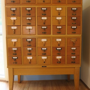 May include: A wooden cabinet with 36 drawers, each with a small label. The cabinet is light brown and has a simple design. The cabinet is on a wooden floor.