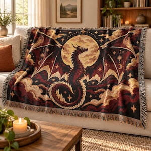 May include: A woven throw blanket featuring a dark dragon silhouette centered against a large, pale yellow full moon. The design includes deep red and black clouds, scattered stars, and a fringed edge, creating a detailed tapestry-style pattern.