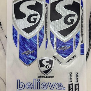 Könnte beinhalten: Ein Bogen mit Cricket-Schläger-Aufklebern, bestehend aus zwei großen schildförmigen Abziehbildern mit blau-silbernen Mustern, dem SG-Logo sowie den Schriftzügen Sanspareils Greenlands, Nexus, Xtreme und believe. become. Enthält weitere kleine Aufkleber.