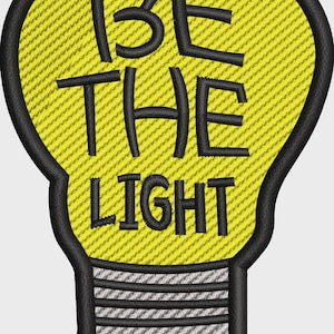 May include: A light bulb shaped embroidered patch with a yellow background and black border. The text BE THE LIGHT is stitched in black across the center. The base of the bulb features horizontal grey and black stripes with a black stitched outline.