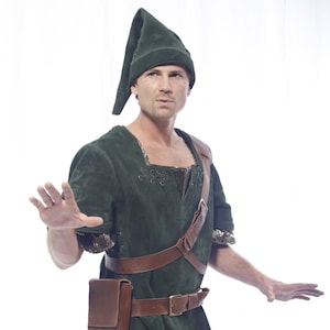 May include: A man wearing a green suede tunic with a brown leather belt and shoulder strap. He is also wearing a green suede hat and brown pants.