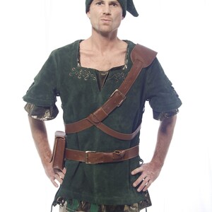 May include: A man wearing a green suede tunic with a brown leather belt and shoulder strap. He is also wearing a green hat with a pointed tip.