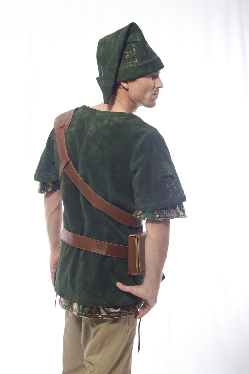 May include: A green suede tunic with brown leather straps and a matching green suede hat with a lace-up detail. The tunic has a brown leather belt and a brown leather pouch.
