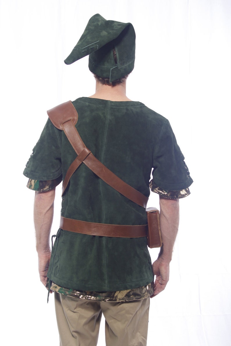 May include: A green suede tunic with brown leather straps and a brown leather belt. The tunic has a camouflage pattern on the sleeves and bottom hem. The person is wearing a green suede hat with a pointed tip.