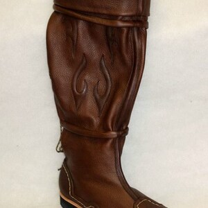 May include: Brown leather knee-high boots with a decorative flame design and a stitched sole.