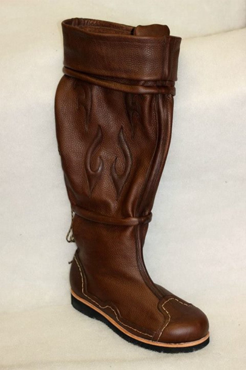 May include: Brown leather knee-high boots with a decorative flame design and a stitched sole.