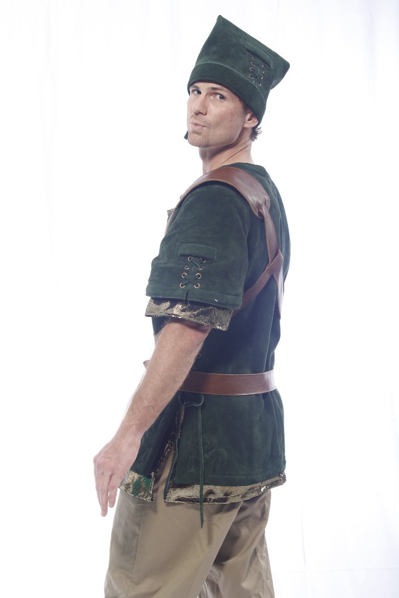 May include: A green suede tunic with brown leather straps and a matching green suede hat. The tunic has a lace-up detail on the sleeve and a brown leather belt.