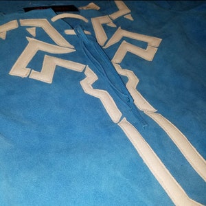 May include: A blue suede shirt with a white geometric design and a white tassel tie.