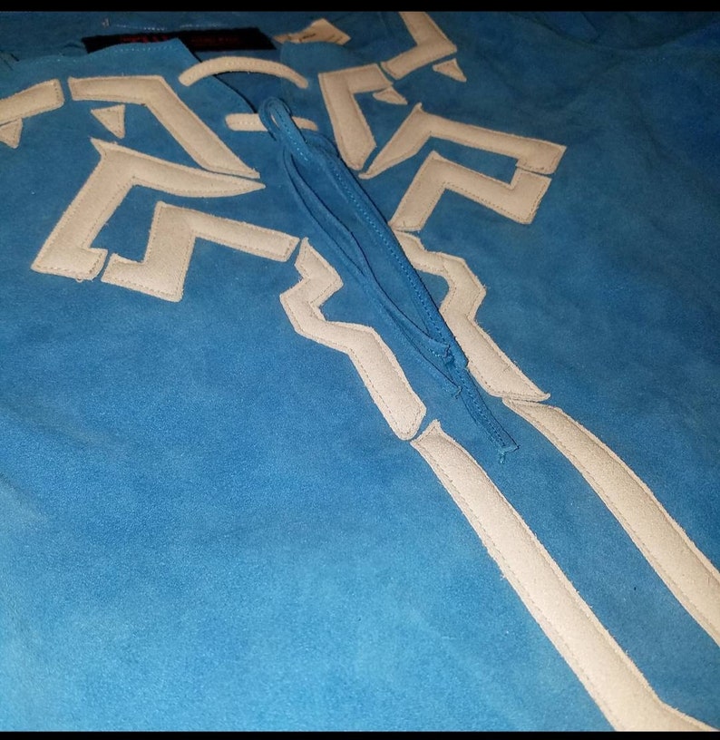 May include: A blue suede shirt with a white geometric design and a white tassel tie.