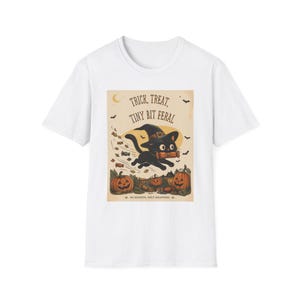 May include: A white short-sleeve t-shirt featuring a graphic of a black cat wearing a witch hat, running with a candy bar. The text reads TRICK, TREAT, TINY BIT FERAL and NO REGRETS, ONLY WRAPPERS, surrounded by pumpkins, bats, and flying candy.