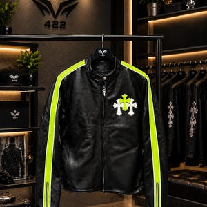 May include: A black leather jacket featuring a stand-up collar, a central silver zipper, and bright neon yellow stripes running down the length of each sleeve. The chest displays a white and neon yellow cross emblem, and the cuffs have zippers.