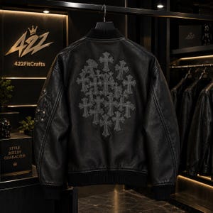 Puede incluir: Una chaqueta bomber de cuero negro con cuello, puños y dobladillo acanalados. La parte posterior muestra un grupo de motivos de cruz bordados en gris oscuro, mientras que la manga presenta un emblema decorativo con detalles de cruz.